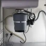 Garbage disposal unit with dark gray exterior and hoses under plumbing for residential installations by Quahog Plumbing.