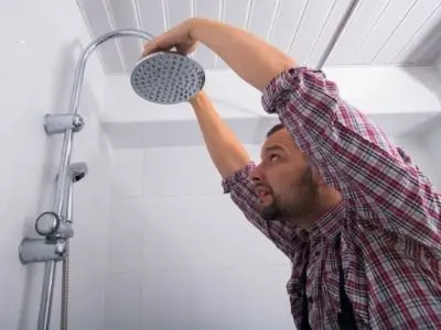 Man inspecting and adjusting a showerhead to address plumbing issues related to water pressure and potential leaks.