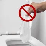 Hand holding a tissue with a red "no" symbol, warning against flushing in a bathroom by Quahog Plumbing.