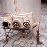 Rusty metal tank or boiler on tiled ground, illustrating aging plumbing equipment by Quahog Plumbing.