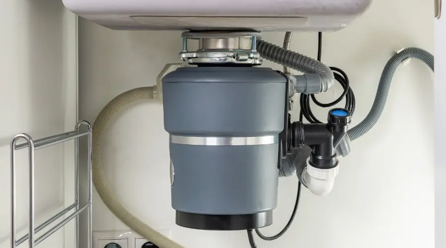 Garbage disposal unit installed under kitchen sink, highlighting plumbing connections and maintenance aspects.
