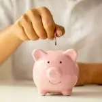 Hand depositing a coin into a cheerful piggy bank, symbolizing savings and financial responsibility for plumbing services.