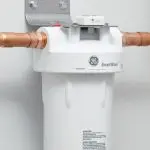 Water filter system with white cylindrical design and copper pipes, installed by Quahog Plumbing for home water purification.
