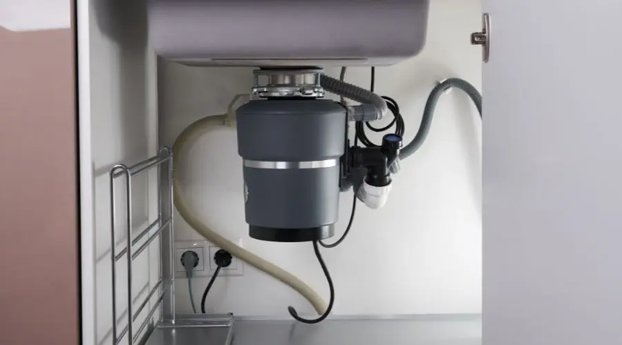 Garbage disposal unit installed under a sink, featuring plumbing components in a dark gray cabinet by Quahog Plumbing.