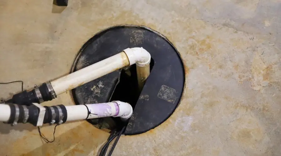 Sump pump and pipes in a circular pit, featuring a worn concrete floor—Quahog Plumbing services plumbing maintenance.
