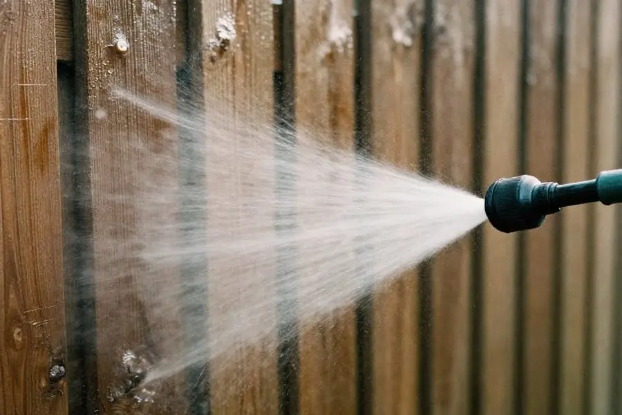 person holding a garden hose and using it to clean a wood fence