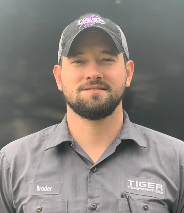 Brader Yelverton, HVAC technician from Tiger Temperature, wearing a uniform and cap, smiling against a dark background.