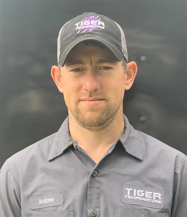Andrew Hebert, HVAC technician at Tiger Temperature, wearing a branded cap and uniform, smiling in front of a dark background.
