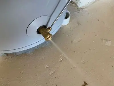Brass valve on a water heater releasing water during flushing process to remove mineral buildup for efficient operation.
