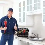 Plumber in a kitchen holding a wrench and giving a thumbs up, showcasing professional plumbing services and expertise.