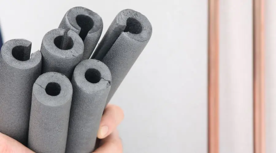 Hand holding multiple foam pipe insulation tubes for protecting plumbing during winter.