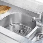 Stainless steel kitchen sink with a modern faucet and a wooden cutting board, illustrating essential plumbing features relevant to drain cleaning services.