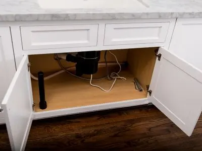 Under-sink cabinet with open doors, showcasing plumbing components including a garbage disposal and exposed pipes, emphasizing the importance of pipe insulation to prevent freezing in colder climates.