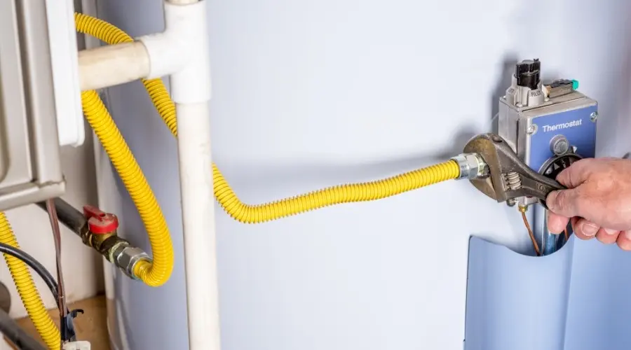 Hand adjusting thermostat on a gas water heater with yellow gas line and plumbing connections, relevant to water heater installation and maintenance topics.