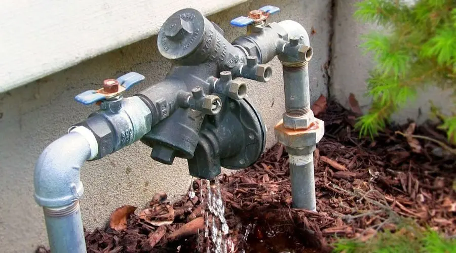 Water meter and pipes showing flowing water and rusty fittings, relating to backflow testing by Hancock & Son Plumbing.