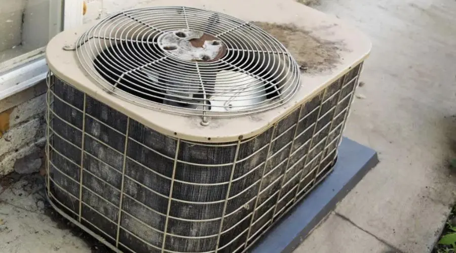Air conditioning unit with rust and dust, beside a building wall, emphasizing HVAC maintenance needs by Hancock & Son.