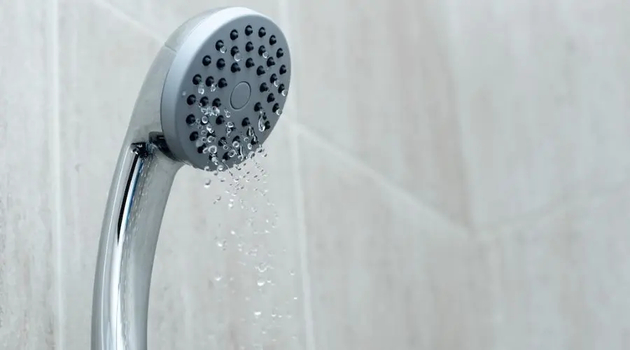 Chrome showerhead with water droplets against tiled background, representing plumbing solutions from Hancock & Son Plumbing.