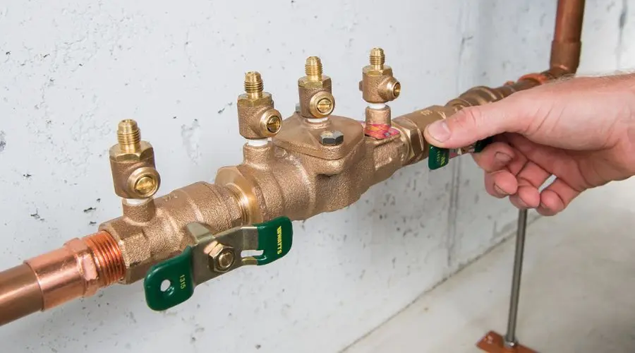 A person's hand adjusting a brass valve on a plumbing system with visible copper piping and green function tags.