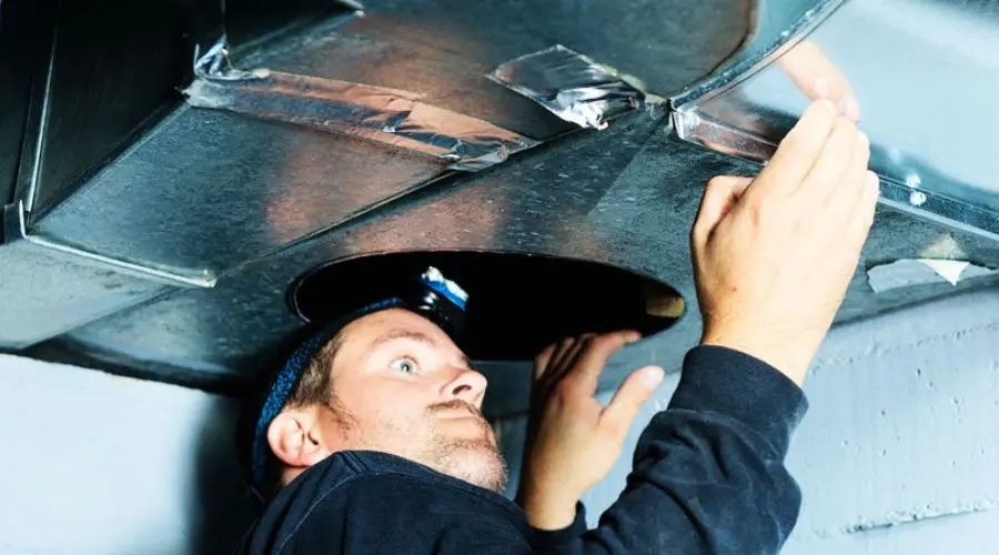 Worker in utility space performing maintenance on metal ductwork for HVAC services by Hancock & Son Plumbing.