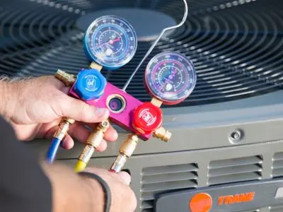 Hands holding pressure gauges connected to an air conditioning unit, illustrating professional maintenance for improved efficiency and reduced repair costs.
