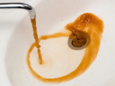 Brown, rust-colored water draining from a sink, indicating potential internal damage in a water heater, relevant to signs of water heater replacement.