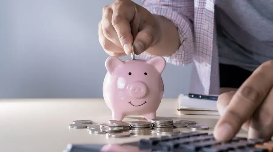 Piggy bank with smiling face, hand inserting coin, calculator for home HVAC financial planning and efficiency.
