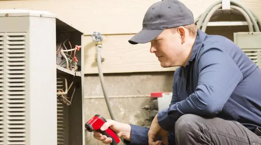 Technician performing maintenance on air conditioning unit with tools in indoor service area of Hancock & Son HVAC.