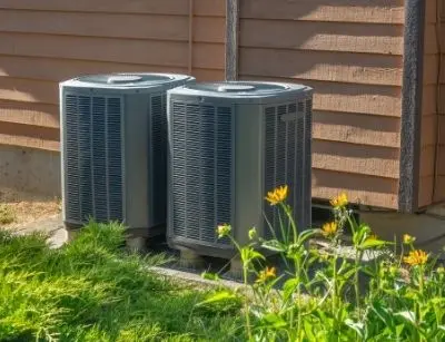 Air conditioning units in a residential setting, surrounded by greenery, emphasizing the importance of proper AC replacement and size selection for efficient cooling.