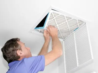 Man changing a ceiling air filter to improve HVAC airflow and efficiency, promoting energy savings and lower electric bills.