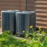 Air conditioning units in a neat outdoor setting with grass and flowers, showcasing efficient HVAC solutions by AirLux.