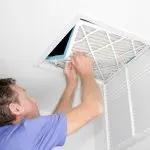 A man maintaining a ceiling access panel and air filter indoors, showcasing HVAC service by AirLux Heating & Cooling.