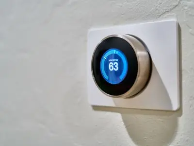 Programmable thermostat displaying a set temperature of 63 degrees Fahrenheit, mounted on a wall, illustrating energy efficiency tips for summer cooling.