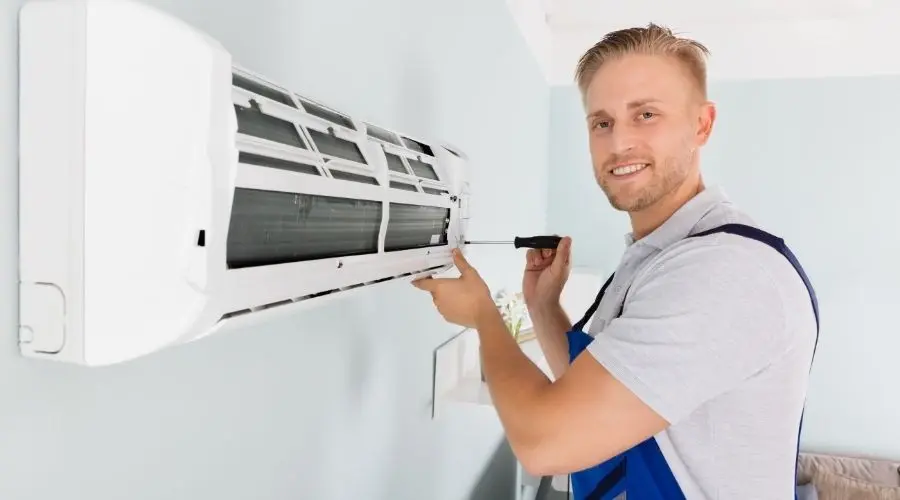 Technician working on air conditioning unit with screwdriver at AirLux Heating & Cooling service location.