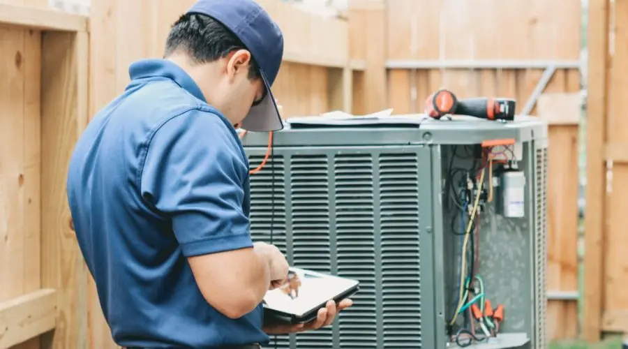 HVAC technician with a tablet servicing an air conditioning unit, representing AirLux Heating & Cooling.