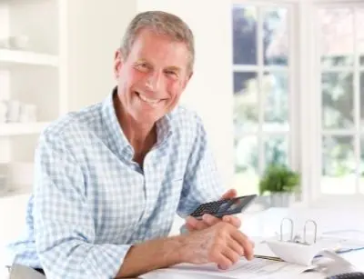 Smiling older man holding a smartphone while reviewing paperwork, representing customer engagement and decision-making for air conditioning services.