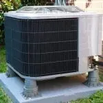 Air conditioning unit on concrete base, surrounded by grass, emphasizing summer HVAC maintenance by AirLux Heating & Cooling.