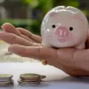 Close-up of a pink piggy bank in hand, with coins on a table, symbolizing financial savings and management.