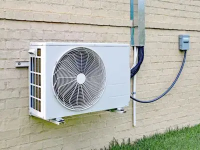 Ductless mini-split air conditioning unit mounted on an exterior wall, featuring a fan and refrigeration lines, illustrating energy-efficient cooling solutions for homes.