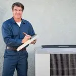 Technician in blue uniform by air conditioning unit, clipboard in hand, representing Jerry Brittingham A/C & Heat services.
