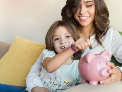 Mother and daughter smiling while saving money in a pink piggy bank, emphasizing the importance of financial planning and security.