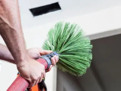 Professional air duct cleaning tool with a green brush attachment, demonstrating the cleaning process to improve indoor air quality and reduce allergens in homes.