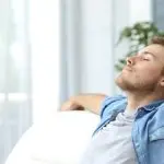 Relaxed young man on comfortable sofa in bright indoor setting, emphasizing HVAC comfort and tranquility.