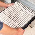 Hands replacing a white pleated air filter in an HVAC unit for Jerry Brittingham A/C & Heat, Inc. maintenance.