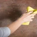 Hand cleaning a wooden surface with a yellow cloth, relevant for HVAC maintenance by Jerry Brittingham A/C & Heat, Inc.
