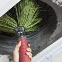 Hand holding a broom with green bristles, cleaning a tire, related to HVAC maintenance by Jerry Brittingham A/C & Heat.