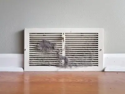 Dusty air vent cover with visible debris and dirt accumulation, indicating potential need for air duct cleaning and maintenance for improved indoor air quality.