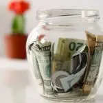 Clear jar filled with cash next to a flower pot, symbolizing savings for HVAC services by Jerry Brittingham A/C & Heat, Inc.