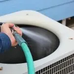 Air conditioning unit cleaned with a hose against a blue wall by Jerry Brittingham A/C & Heat, Inc.