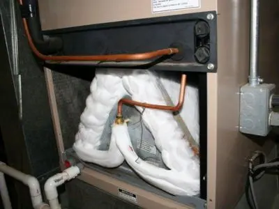 Frozen evaporator coils in an air conditioning unit, with visible frost buildup on the coils and copper refrigerant lines, indicating potential refrigerant leak issues.