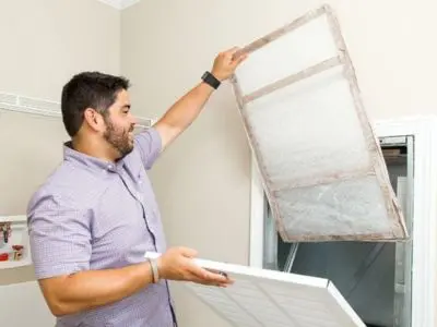 Man replacing a dirty air filter, illustrating HVAC maintenance tips for improving indoor air quality and duct cleanliness.